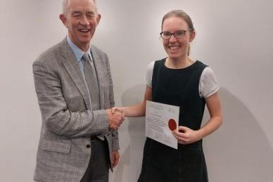 woman holds certificate whilst shaking hands with man on left